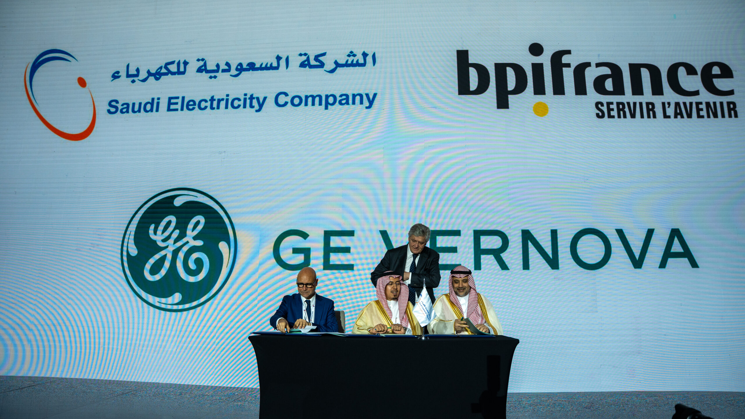 A signing on stage beneath the Saudi Electricity Company, bpifrance and GE Vernova marks